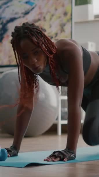 Вертикальное видео: подтянутая чернокожая женщина в спортивном костюме тренируется сжигать жировые калории, тренируя силу, тренируя фитнес на аэробической карте в гостиной. Взрослый спортсмен, наслаждающийся здоровым образом жизни - Кадры, видео