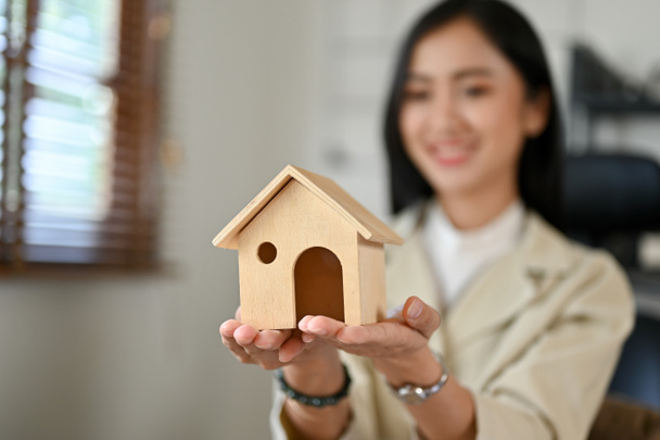 Una hermosa mujer asiática agente de bienes raíces o agente de bienes raíces sosteniendo un modelo de casa. Imagen de primer plano y enfoque selectivo - Foto, imagen