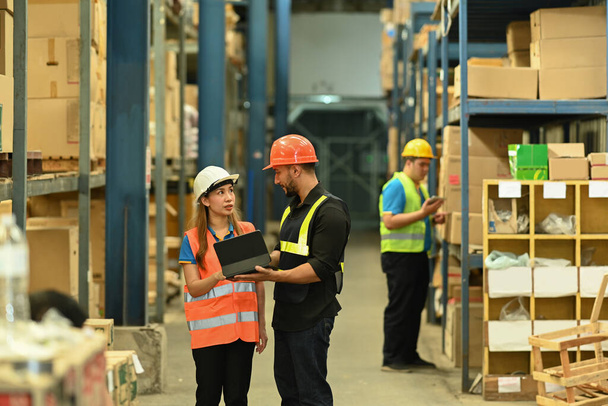 Full length of two warehouse workers are standing between retail warehouse full of shelves and checking order details on a tablet. - Photo, Image