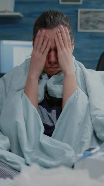 Verticale video: Close-up van zieke persoon wrijven tempels om hoofdpijn te genezen terwijl zitten verpakt in deken. Portret van een volwassene met griepsymptomen met migraine en hand op hand. Vrouw met - Video