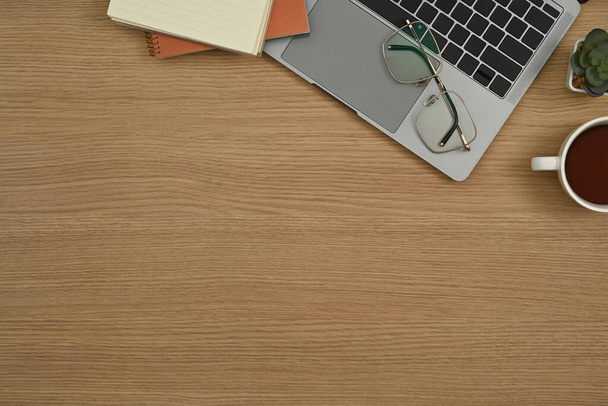Posto di lavoro semplice con computer portatile, occhiali, blocco note e tazza di caffè su sfondo di legno.  - Foto, immagini