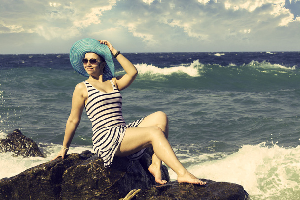 Beautiful woman sitting on a stone and splashing in the sea. Vintage style - Foto, afbeelding