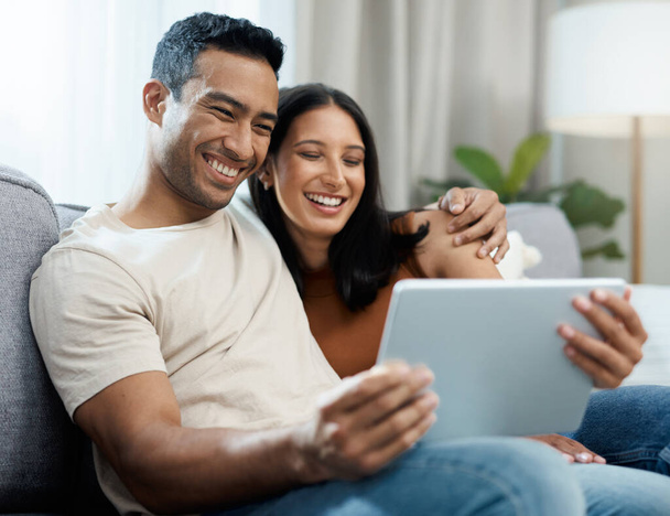 Este es nuestro momento para relajarnos. una joven pareja sentada en el sofá juntos en casa y usando una tableta digital - Foto, imagen