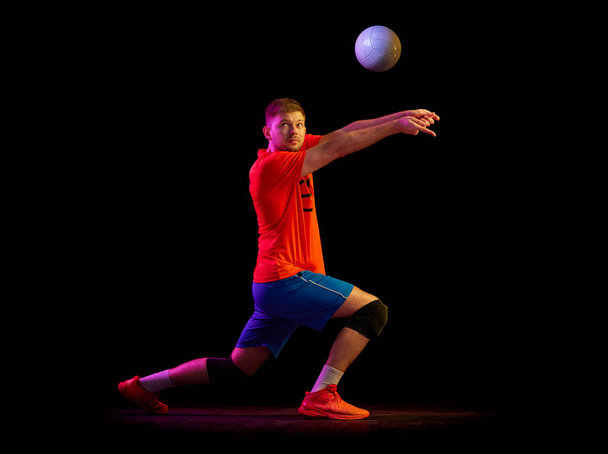 Dynamic portrait of male volleyball player training with ball isolated on dark background in neon light. Sport, gym, team sport, challenges. Athlete playing volleyball - Foto, Imagem