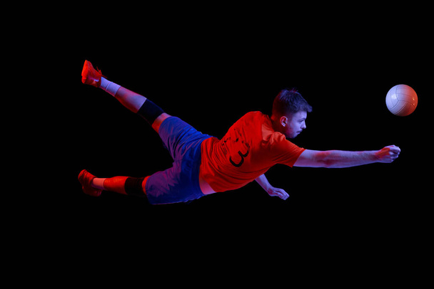 Flight. Young man, professional volleyball player in sports uniform in jump with ball isolated on dark background. Sportive man playing volleyball. Action, sport, health, team, fitness concept - Fotoğraf, Görsel