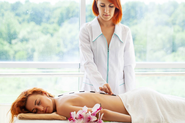 Professionelle Kosmetikerin massiert weiblichen Rücken mit Steinen im Schönheitsstudio. - Foto, Bild