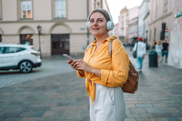 Gelukkig Kaukasische vrouw in goed humeur is gekleed casual zomerkleding luisteren naar muziek en kijken naar het telefoonscherm. Positieve emotie concept - Foto, afbeelding