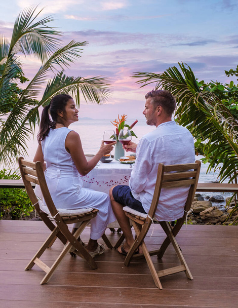 pariskunta romanttisella illallisella meren äärellä, ruokapöytä katselemassa merelle thairuoan kanssa, illallinen auringonlaskun aikana. romanttinen illallinen Thaimaassa - Valokuva, kuva