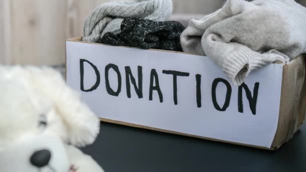 4k zoom in out Donation box with old used toys and clothes indoors. Happy Charity. Box with clothes in it. close-up. Clothing donation. Winter clothes in a cardboard box. Seasonal clothing - Video, Çekim