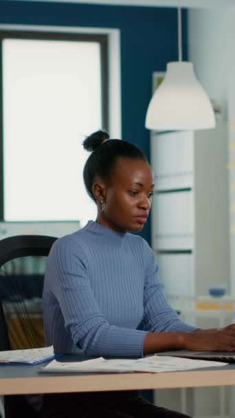 Портрет усміхненої афро-американської жінки, яка працює з доходами і продає статистику за допомогою ноутбука, який сидить за столом в офісі стартапу. Працівники бізнесу, задоволені результатом роботи.. - Кадри, відео