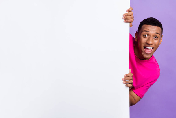 Photo of cheerful nice man wear stylish pink clothes hand hold empty space head behind big board isolated on purple color background. - Zdjęcie, obraz