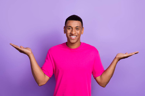 Portrait d'homme rayonnant de dents avec coiffure décolorée porter des paumes de t-shirt rose démontrant l'espace vide isolé sur fond de couleur violette. - Photo, image