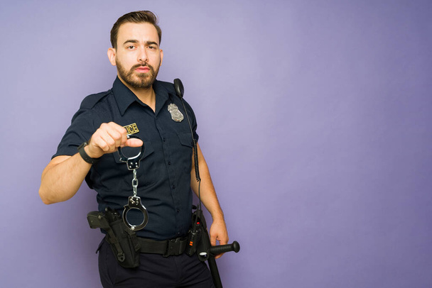 Verärgerter Polizeiagent schaut wütend, während er Handschellen hält, um einen Kriminellen neben dem Kopierraum zu verhaften - Foto, Bild