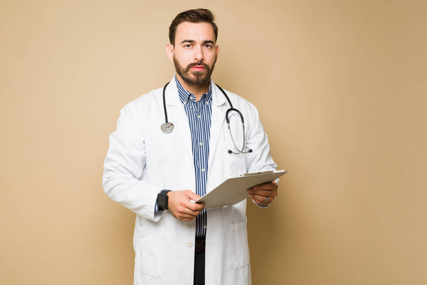 Mężczyzna zestresowany lekarz stetoskopem trzymający schowek z kartoteką medyczną pacjenta - Zdjęcie, obraz
