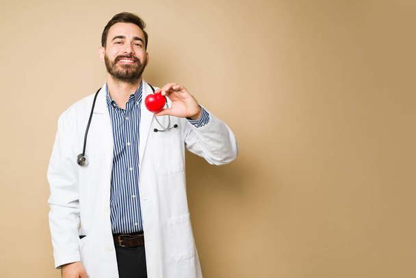 Allegro medico cardiologo che sembra felice sorridente mentre tiene un cuore rosso sano - Foto, immagini