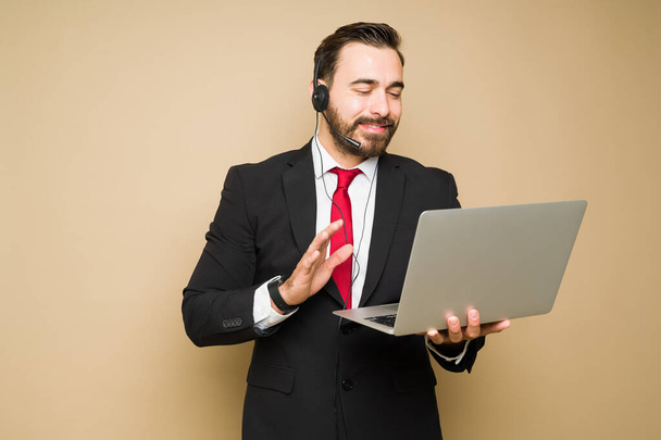 Przystojny biały przedstawiciel handlowy uśmiechnięty podczas korzystania z laptopa pracującego w call center - Zdjęcie, obraz