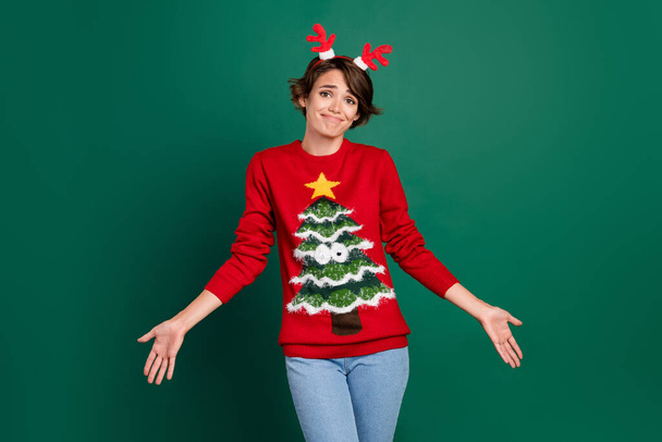 Photo of cute funky lady wear red sweater looking horns hair band shrugging shoulders isolated green color background. - Foto, Bild