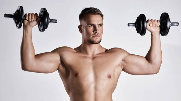 Just lift those doubts away. a sporty young man working out with dumbbells against a grey background - Foto, Bild