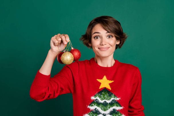 Photo of sweet funky girl dressed ugly print pullover holding colorful tree decorations isolated green color background. - Fotó, kép