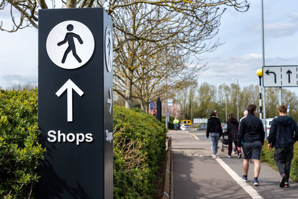 Multidirektionales Wegweiser-Schild mit Pfeil und Fußgänger-Symbol, das auf dem Fußweg in Richtung städtische Einkaufsmeile zeigt. Menschen im Hintergrund auf dem Weg.  - Foto, Bild