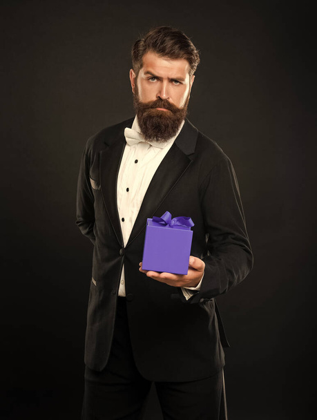serious man in tuxedo bow tie formalwear on black background with box. shopping sale. - Zdjęcie, obraz
