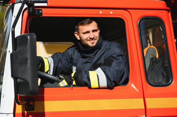Portrait of happy young fireman driving firetruck at station. - Fotografie, Obrázek
