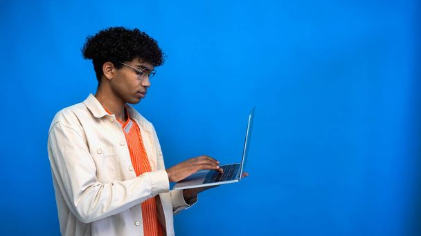 Fiatal afro-amerikai szabadúszó szemüveges laptop elszigetelt kék  - Fotó, kép
