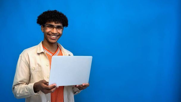 Smiling african american freelancer looking at camera and holding laptop on blue background  - Foto, Imagen