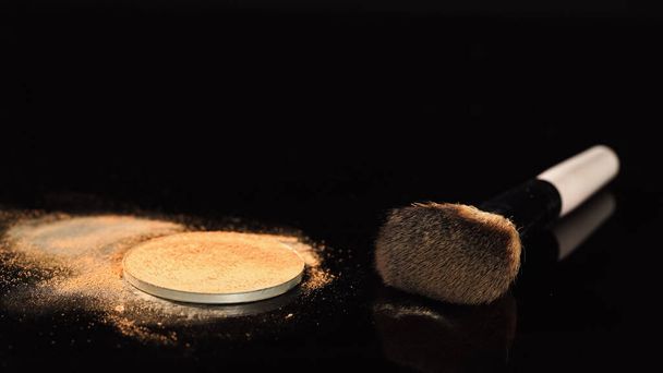 Spazzola cosmetica vicino alla polvere beige su superficie nera  - Foto, immagini