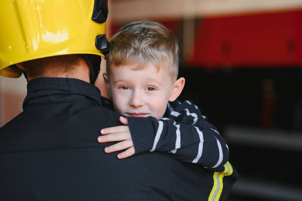 Portrait of rescued little boy with firefighter man standing near fire truck. Firefighter in fire fighting operation - Foto, Imagem