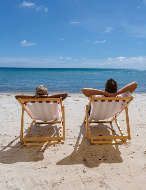 南国の島、コ・コッド・タイの椅子と青い空を持つビーチバケーションのコンセプト。カラフルなビーチチェアでビーチでリラックスした男性と女性 - 写真・画像