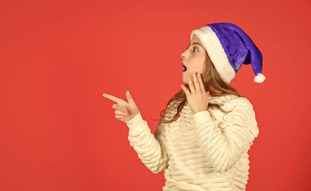Christmas holiday invitation. Adorable girl wear santa claus hat red background. Emotional face expression. Happy childhood. Counting days till christmas. Christmas party. Can not hold back emotions. - Φωτογραφία, εικόνα