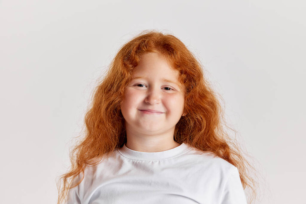 Smiling child. Cute little girl, kid with long curly red hair looking at camera isolated over white background. Concept of children positive emotions, beauty, facial expressions. Copy space for ad - Photo, image