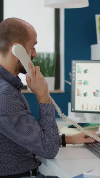 Κάθετη βίντεο: Γραμματέας της εταιρείας μιλώντας στο σταθερό τηλέφωνο στο γραφείο, εργάζονται σε επιχειρηματικό σχέδιο με διαγράμματα και γραφήματα. Υπάλληλος γραφείου συζητά σχετικά με τη στρατηγική τηλεφωνικής επικοινωνίας και προγραμματισμού. - Πλάνα, βίντεο