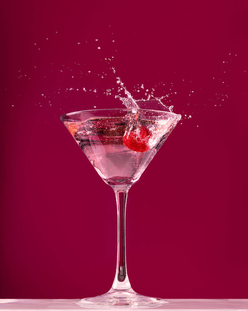 Salpicadura de frambuesa en una copa de cóctel de martini sobre fondo rojo oscuro - Foto, imagen