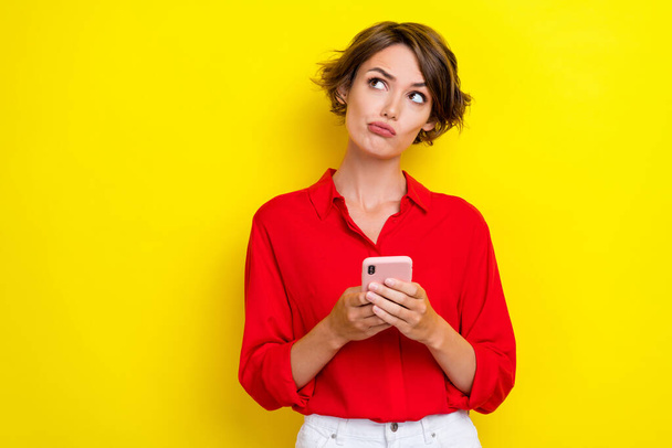 Portrait of positive thoughtful girl with bob hairstyle wear red shirt writing post in social media isolated on yellow color background. - Фото, зображення