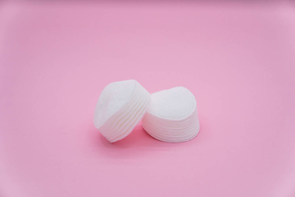 Almohadillas de algodón blanco para limpiar. Una pila de suaves almohadillas de algodón sobre un fondo rosa. - Foto, imagen