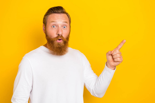 Photo of young funny face redhair man pouted lips speechless reaction directing finger empty space offer isolated on yellow color background. - Zdjęcie, obraz