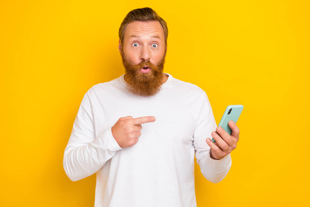 Portrait photo of young attractive funny grimace red hair guy mustache finger directing phone new app software isolated on yellow color background. - Фото, изображение