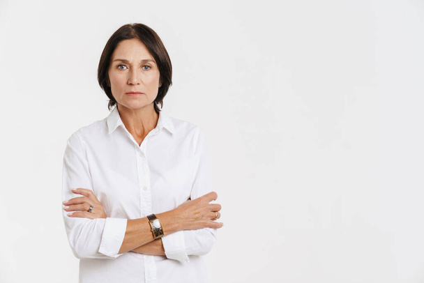 Mature woman looking at camera while posing with arms crossed isolated over white background - Фото, изображение