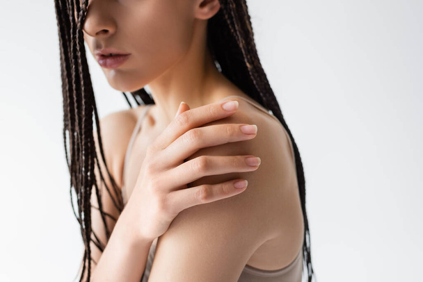 Cropped view of young woman with braids touching shoulder isolated on grey  - Foto, Bild