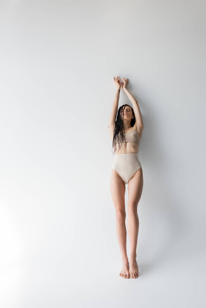 Full length of young fit woman in underwear standing with closed eyes on grey background  - Photo, Image