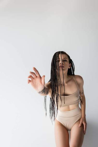 Fit woman with braids outstretching hand at camera on grey background  - Foto, Imagem