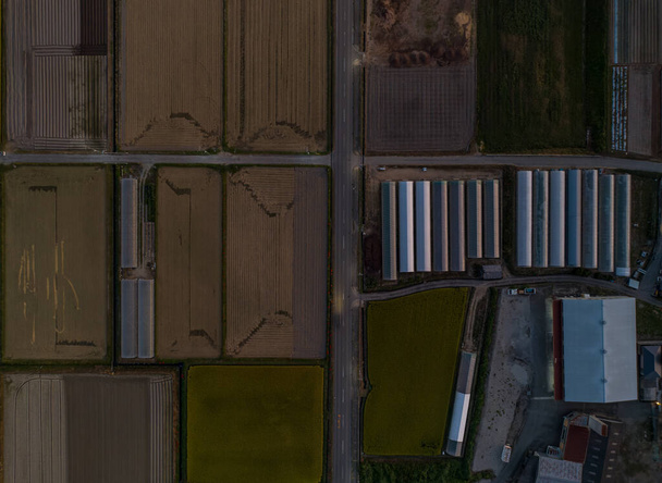 Felülről lefelé néző ültetetlen mezők és üvegházak a gazdaságban alkonyatkor. Kiváló minőségű fénykép - Fotó, kép