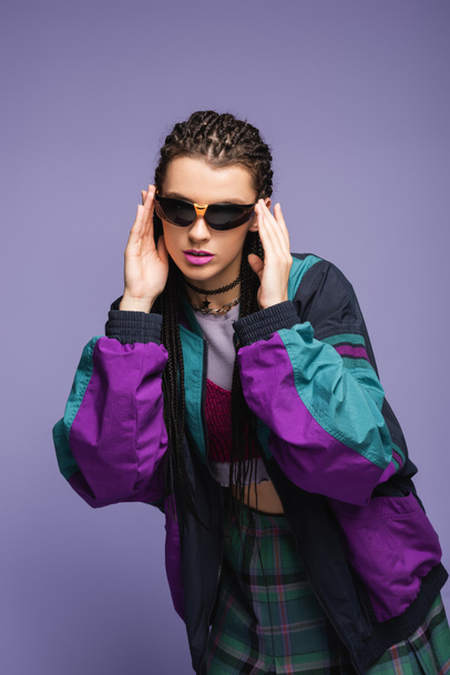 Stylish model in sunglasses and retro sports jacket isolated on purple  - Fotoğraf, Görsel
