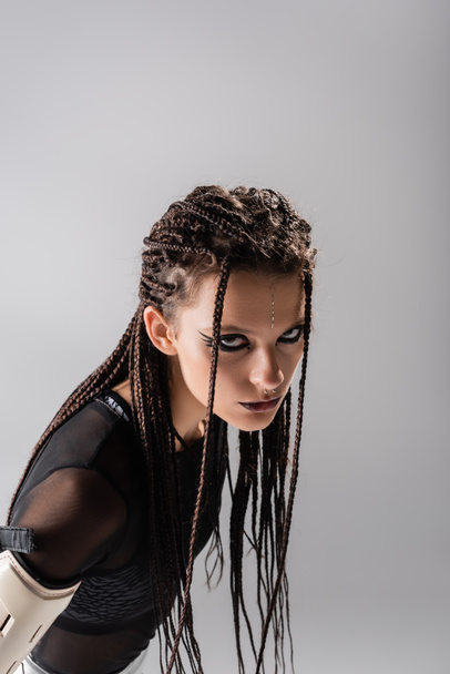 young woman with braids and futuristic outfit looking at camera isolated on grey - Foto, immagini