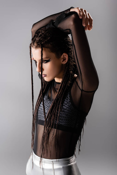 futuristic style woman with dreadlocks posing with hands above head isolated on grey - Foto, Imagem