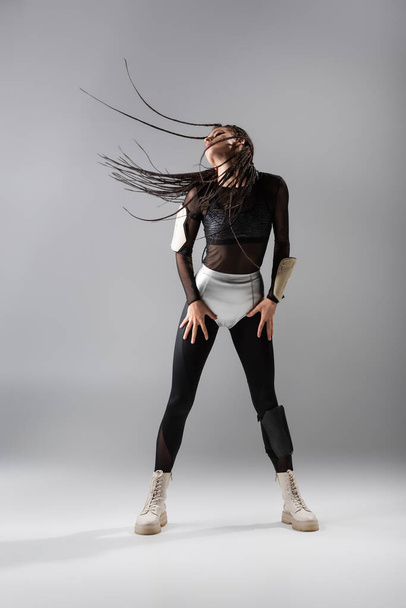 full length of fit woman with dreadlocks posing in black jumpsuit and silver shorts on grey background - Foto, Imagem