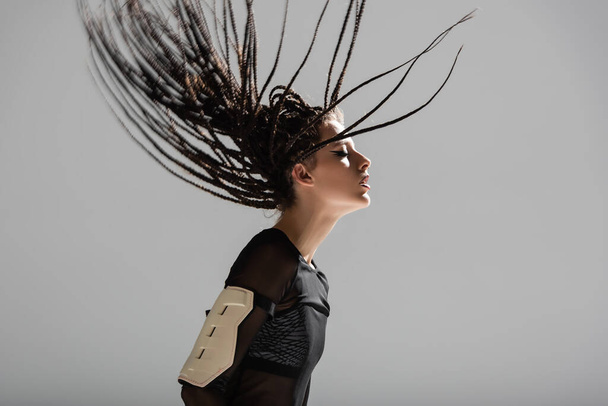 side view of futuristic style woman with braided dreadlocks posing isolated on grey - Foto, Bild