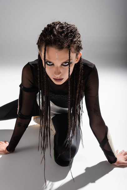 futuristic style woman with dreadlocks posing in black tight jumpsuit on grey background - Foto, Imagen